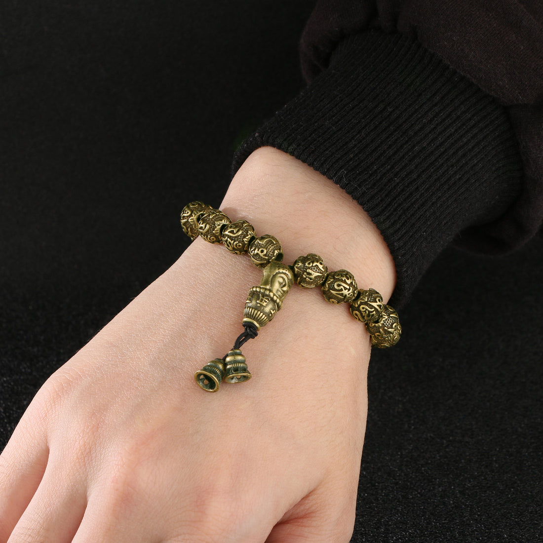 The antique brass Amitabha Buddha stacking bracelet worn with other rings on a wrist.