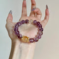Purple Aura Quartz chakra bracelet held in hand, showcasing the white and yellow beads for balance and manifestation.