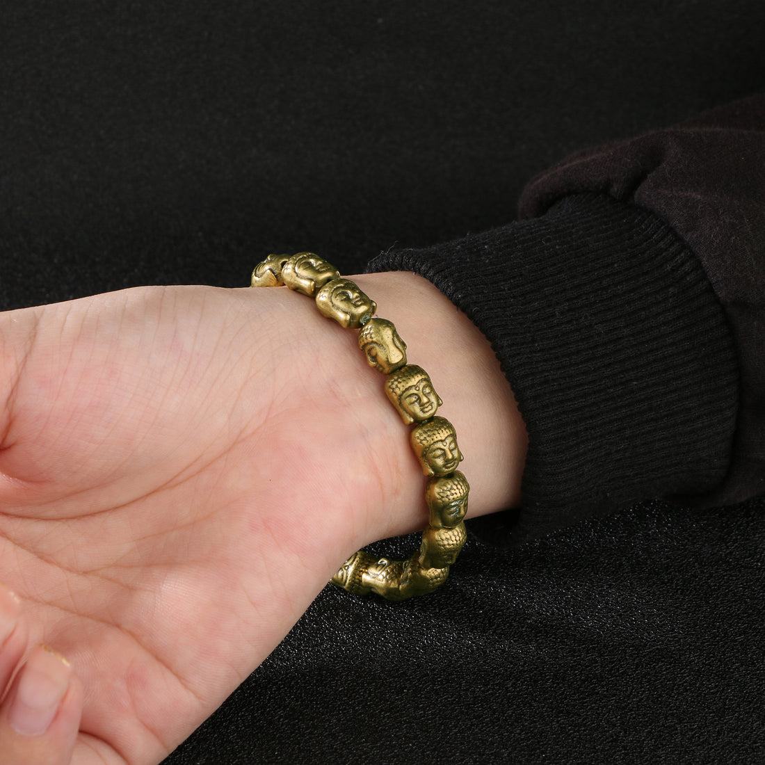 The antique brass Amitabha Buddha stacking bracelet worn with other rings on a wrist.